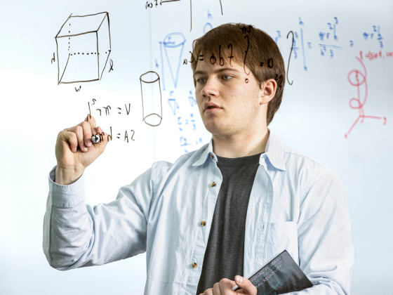 Zane Nordwick writing math equations on a glass wall. | MSU Photo by Marcus “Doc” Cravens