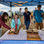 People stand beneath a blue tent looking at bread samples