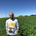 A man stands in a field in front of a blue sky