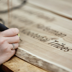 A detail view of text being written with a wood burning pen on a wood panel.