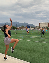 A person wearing shorts and a tank top is punching the air with one foot lifted up. people on the field across from her mimick her actions