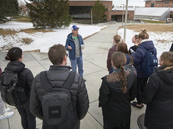A group stands around a male tour guide in front of a brick building and a snowy lawn. | MSU Photo by Colter Peterson