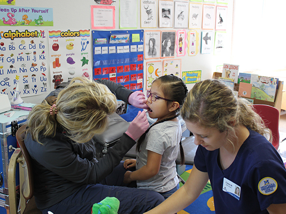 a dental hygienist examines a child's teeth in a classroom while a nursing student assists | Submitted photo