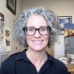 A woman with curly hair and wearing glasses smiles in this head-and-shoulders portrait.