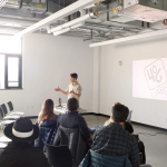 One person speaks in front of a group in a classroom with the words 
