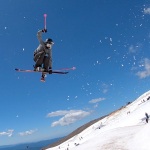 A skier flying through the air with a blue sky in the background.