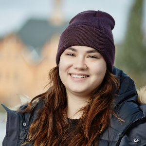 A woman in a black down jacket and beanie stands outside of Montana Hall for a portrait.
