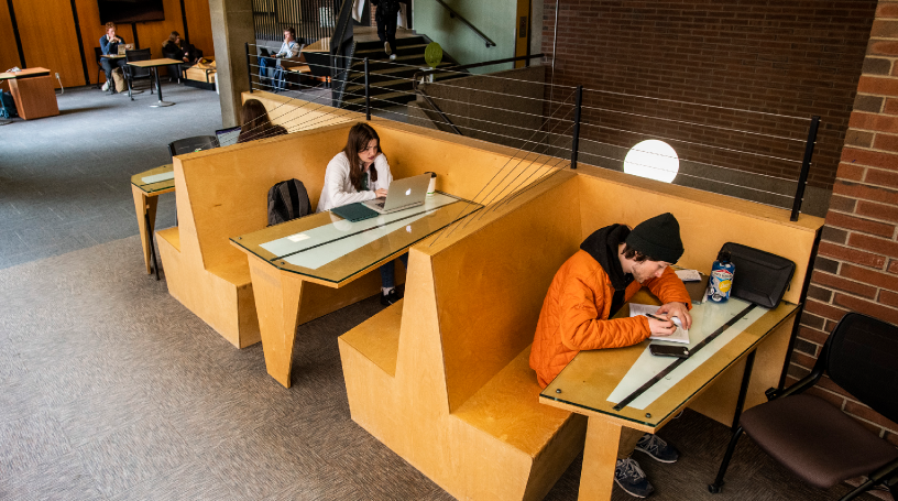 students on computers and studying at wood tables and benches indoors