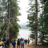 People waling down a forested trail towards a lake