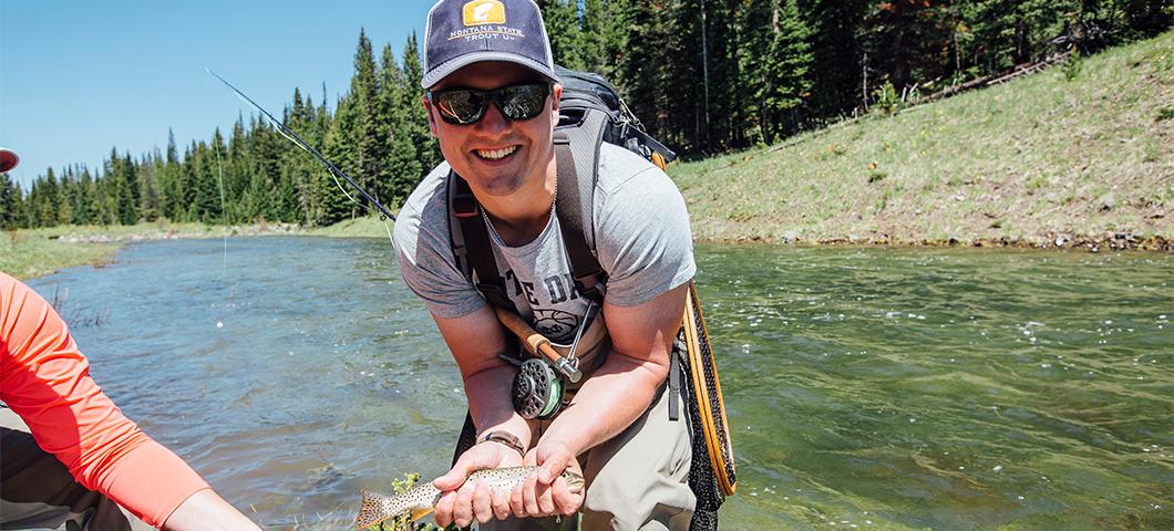 Young male posing for photo while holding a fish he caught in a creek