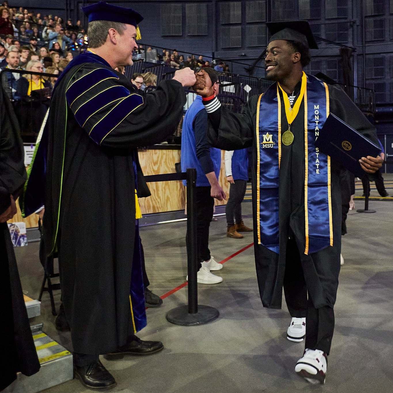 Student fist bumps a professor at MSU's Commencement Exercises in the Brick Breeden Fieldhouse
