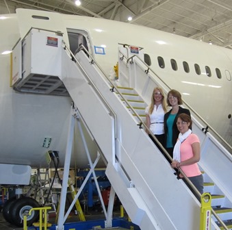 Three students stand on stairs leading up to an airplane