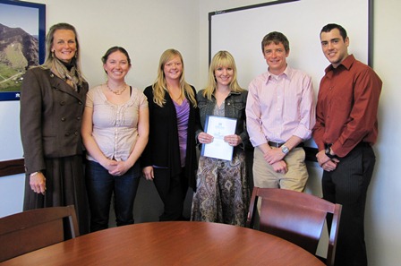 Six people stand in a small conference room