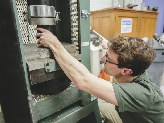 a student reaches up into a device used for crushing concrete cylinders to test their strength