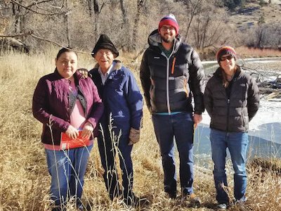 Two Crow tribal members stand beside two MSU researchers beside stream.