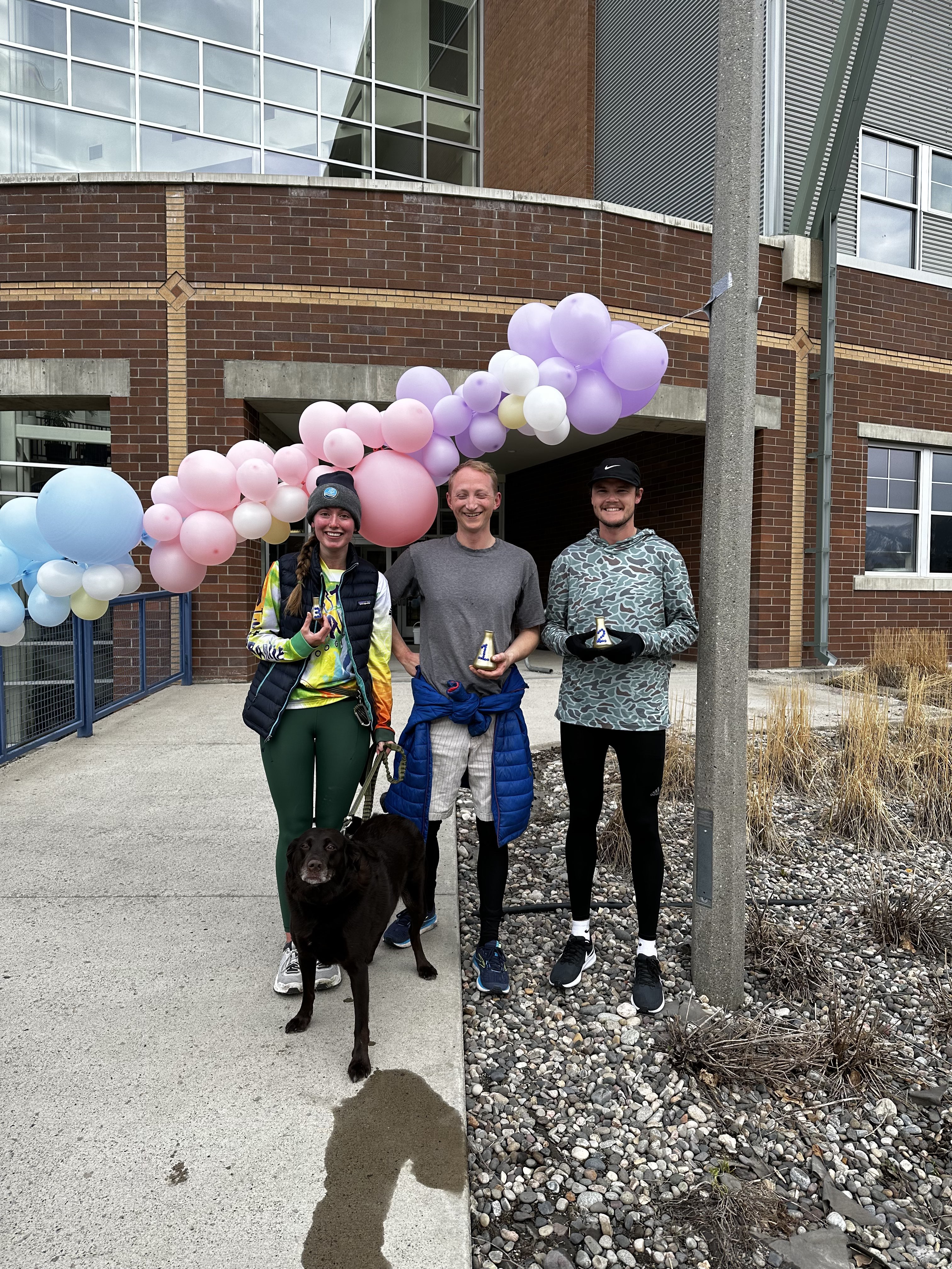 3 grad students and dog pose with trophies from fun run