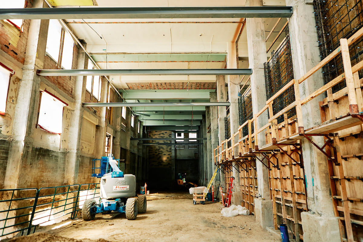 A hallway in a partially demolished building undergoing major renovation. Exposed bricks, floorboards and construction equipment are seen.