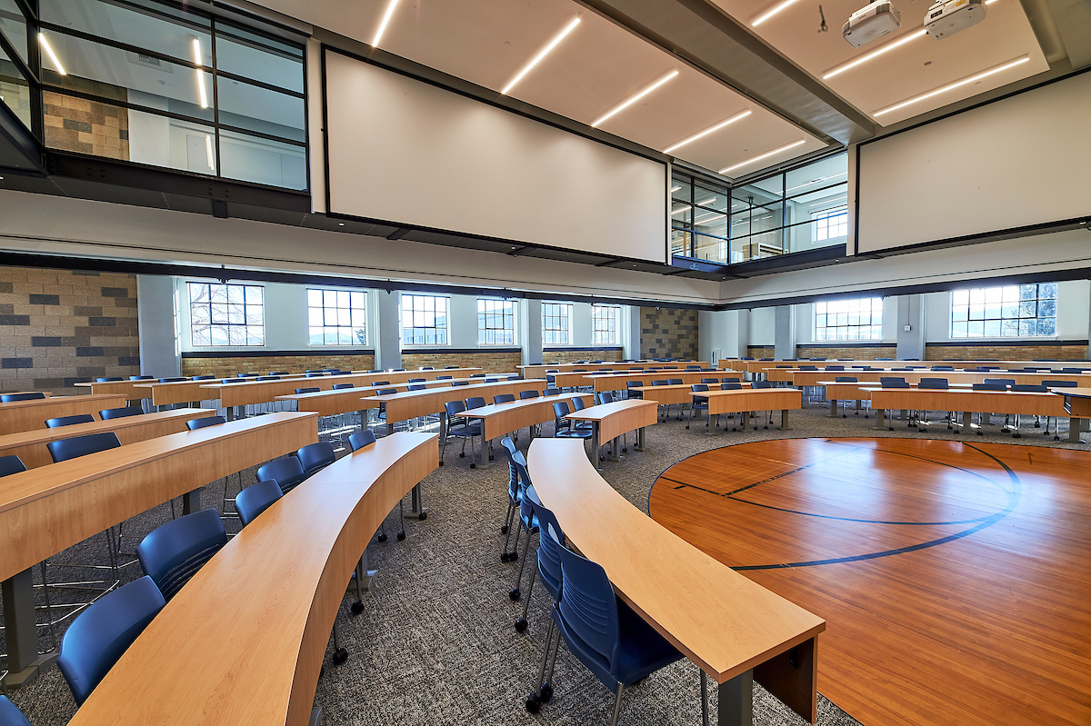 A classroom in the round in a modern academic building. Part of the floor in the foreground is made from the planks of an old basketball court.