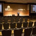 Classroom style seating. Lights are dimmed. Montana State University “GOBO” and a mountains “GOBO” is projected onto the wood panel wall. Projector screens are down. A lectern and microphone are on the former stage. View is from the back of the room.
