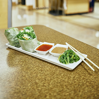 spring rolls, dipping sauce, and seaweed salad on a white plate with chopsticks