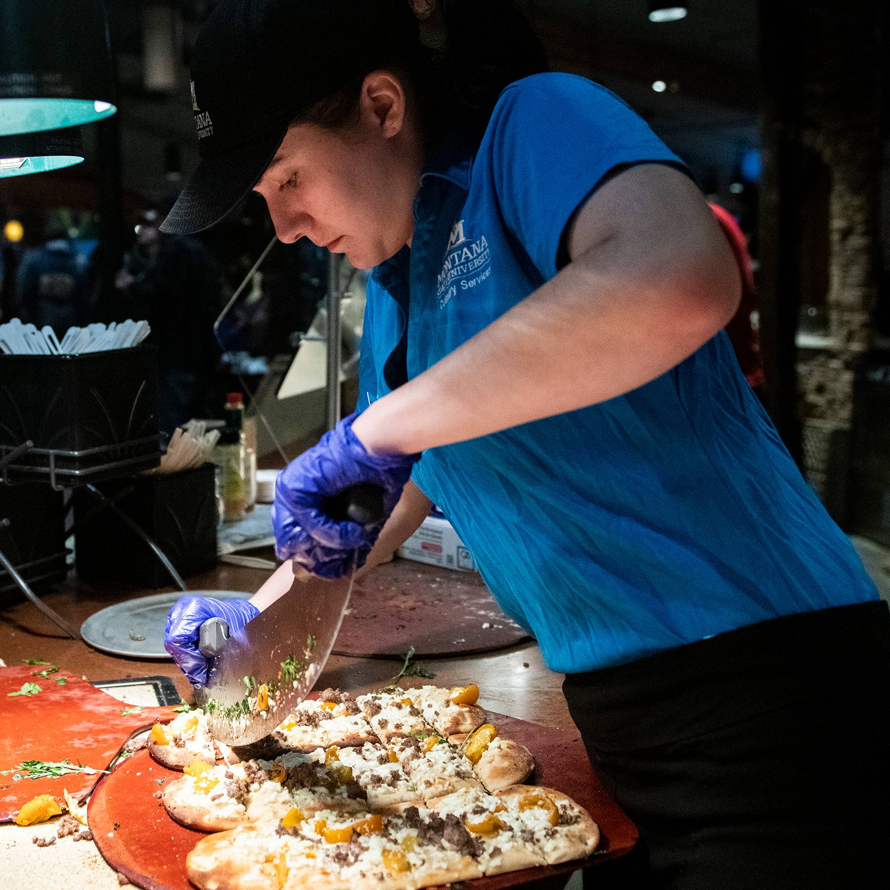 student worker cutting pizza