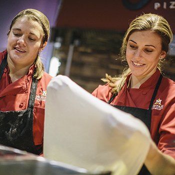 two female culinary services workers stretching pizza dough