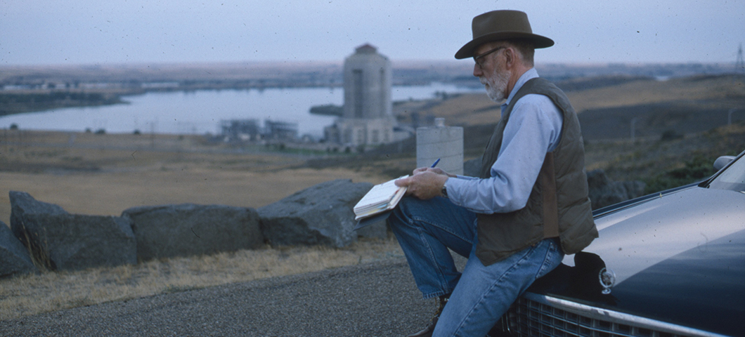 Ivan Doig sitting on hood of Cadillac writing