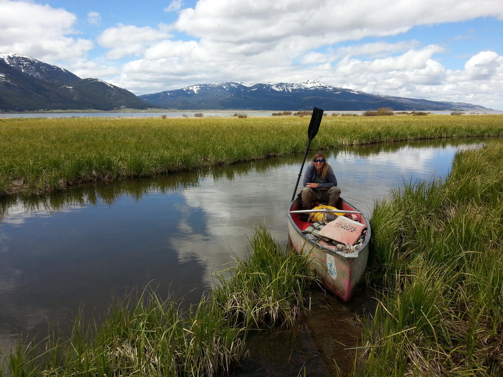 Kristen in a canoe on a small river with snowcapped mountains in the background