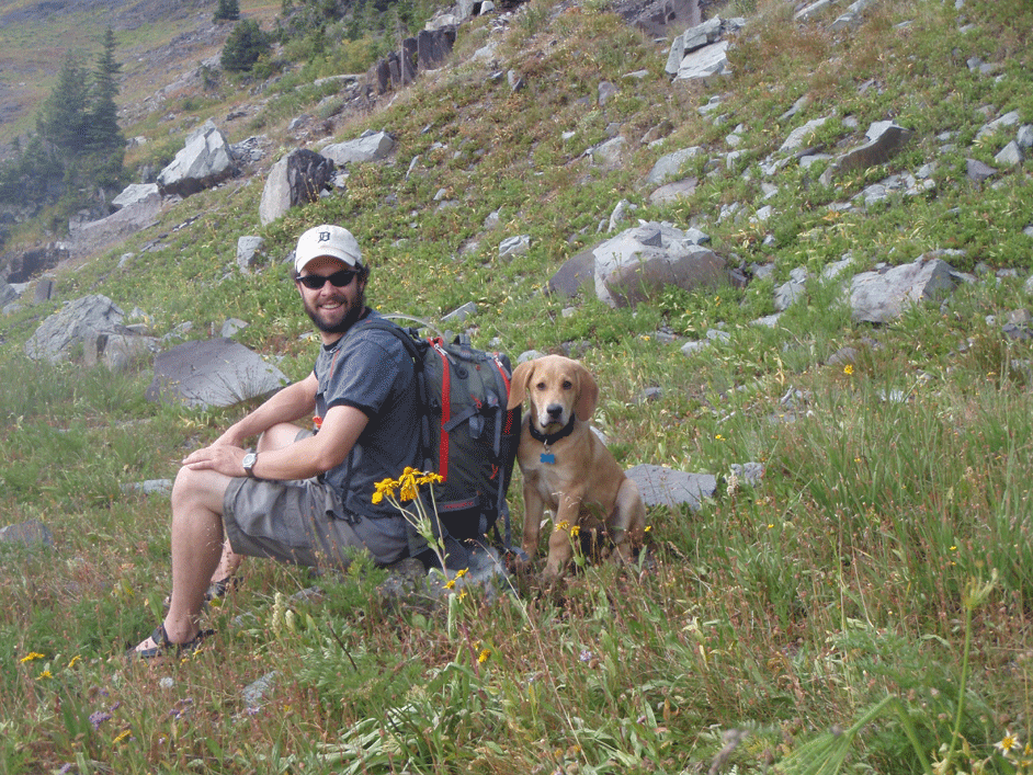 Anthony sitting in a mtn field with dog