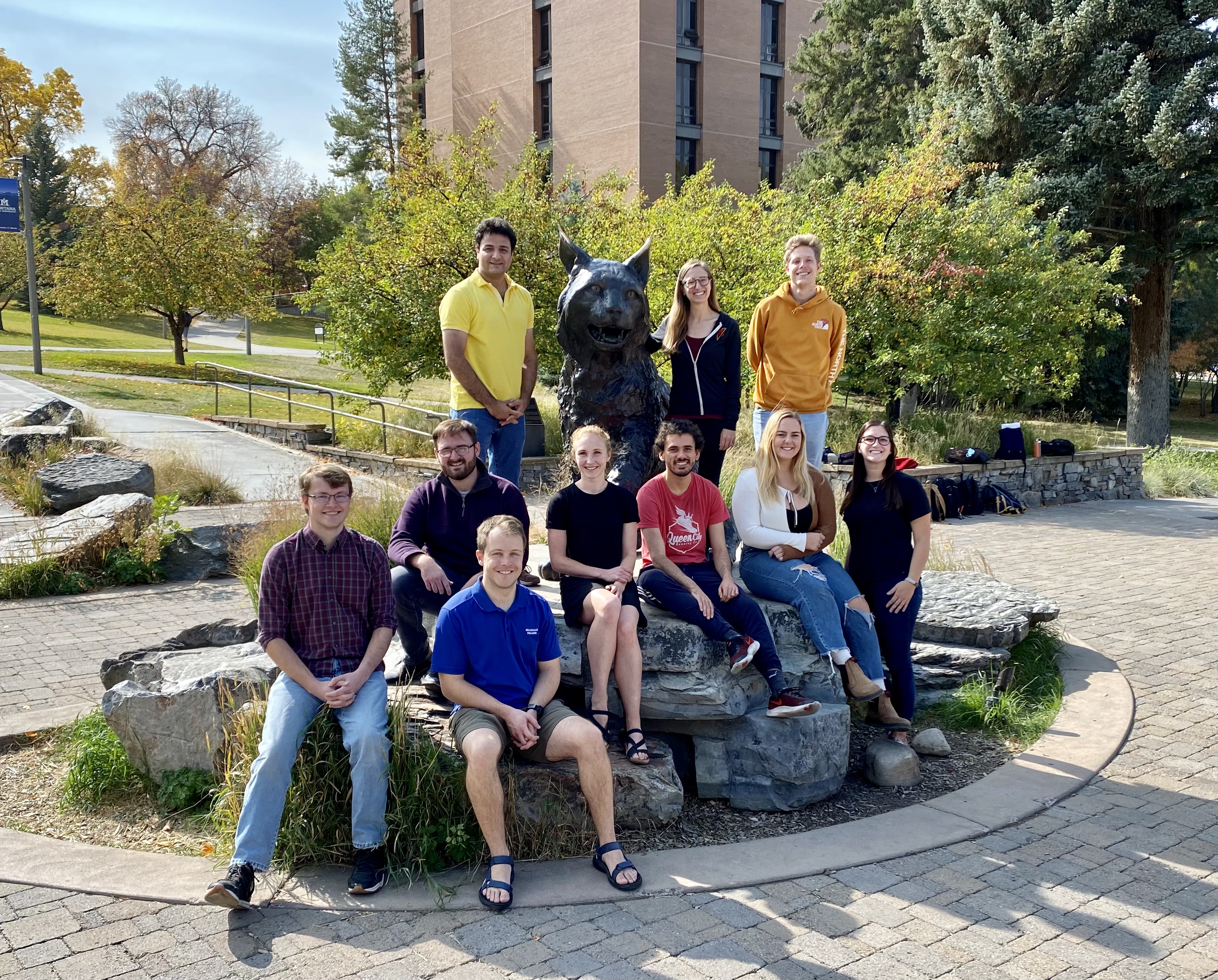 A diverse group of graduate students surround the Champ bobcat statue.