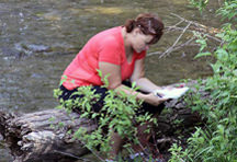 Photo: Student Reading By Stream