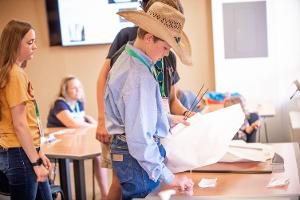 boy with cowboy hat stadning at a table