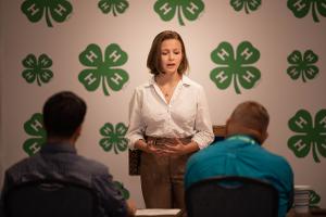 girl in front of clover backdrop giving a speech