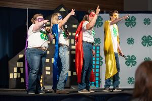 4 youth on stage with super hero capes