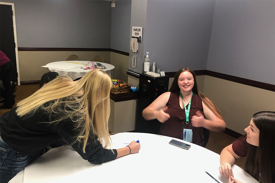 girl at a table working and girl smiling at he camera