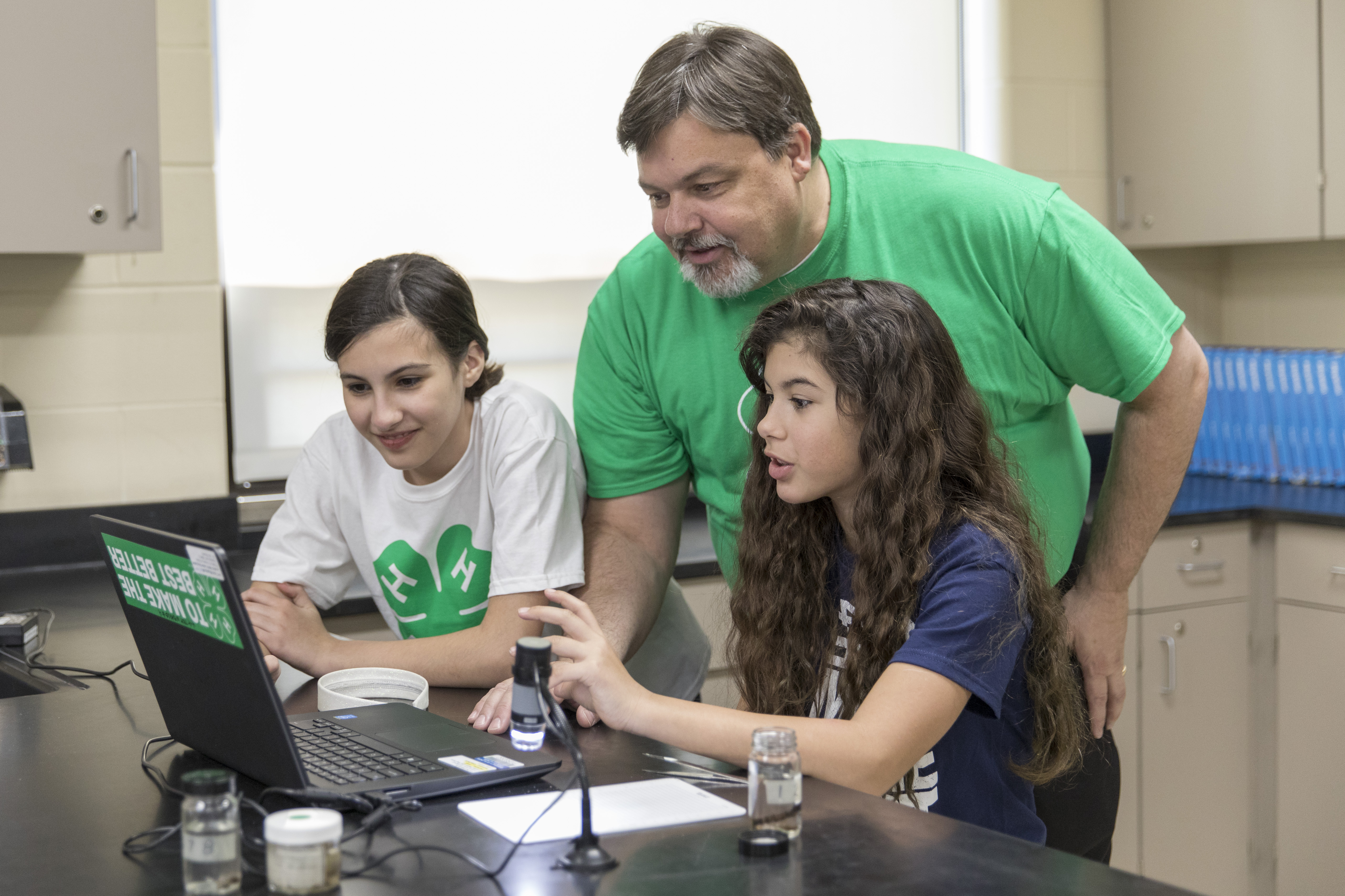 A male volunteer assists two 4-H members on a computer.