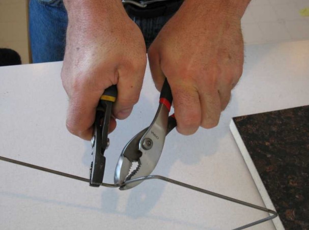 Hands holding two pairs of pliers form a pistol hook out of a steel rod.