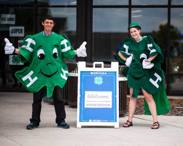 boy and girl dressed like 4-H clover stadning in front of event welcome sign.