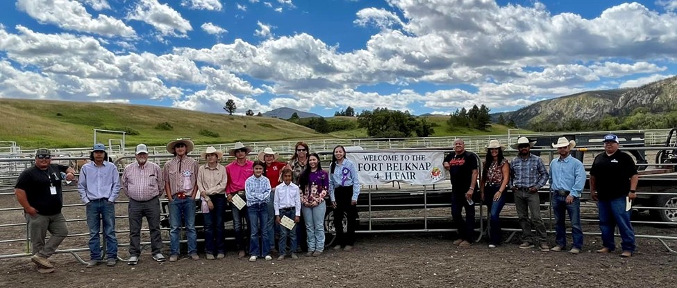 4H members stand in front of the panels of the riding arena at the fair. 