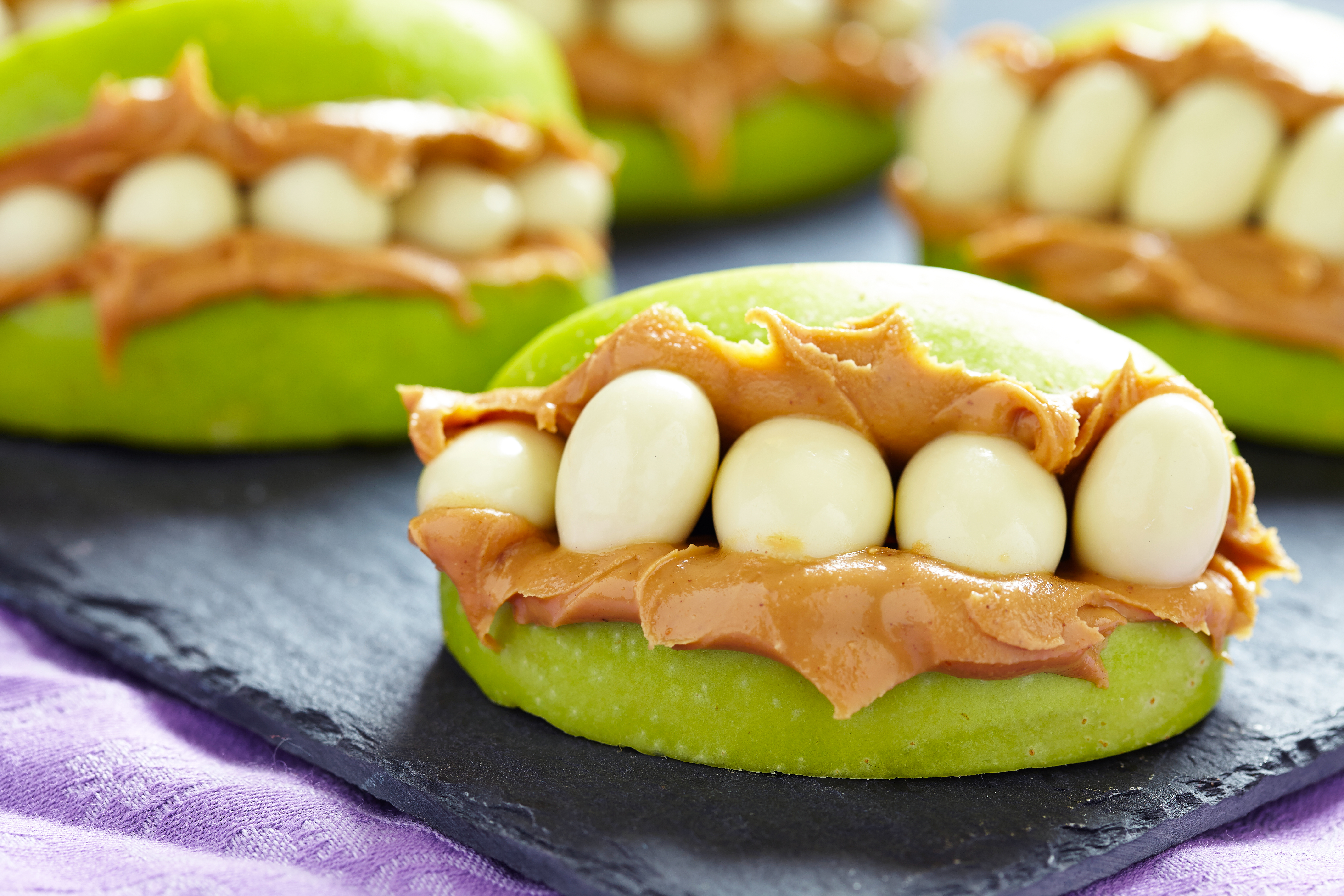 Peanut butter and yogurt covered raisins between green apple slices.