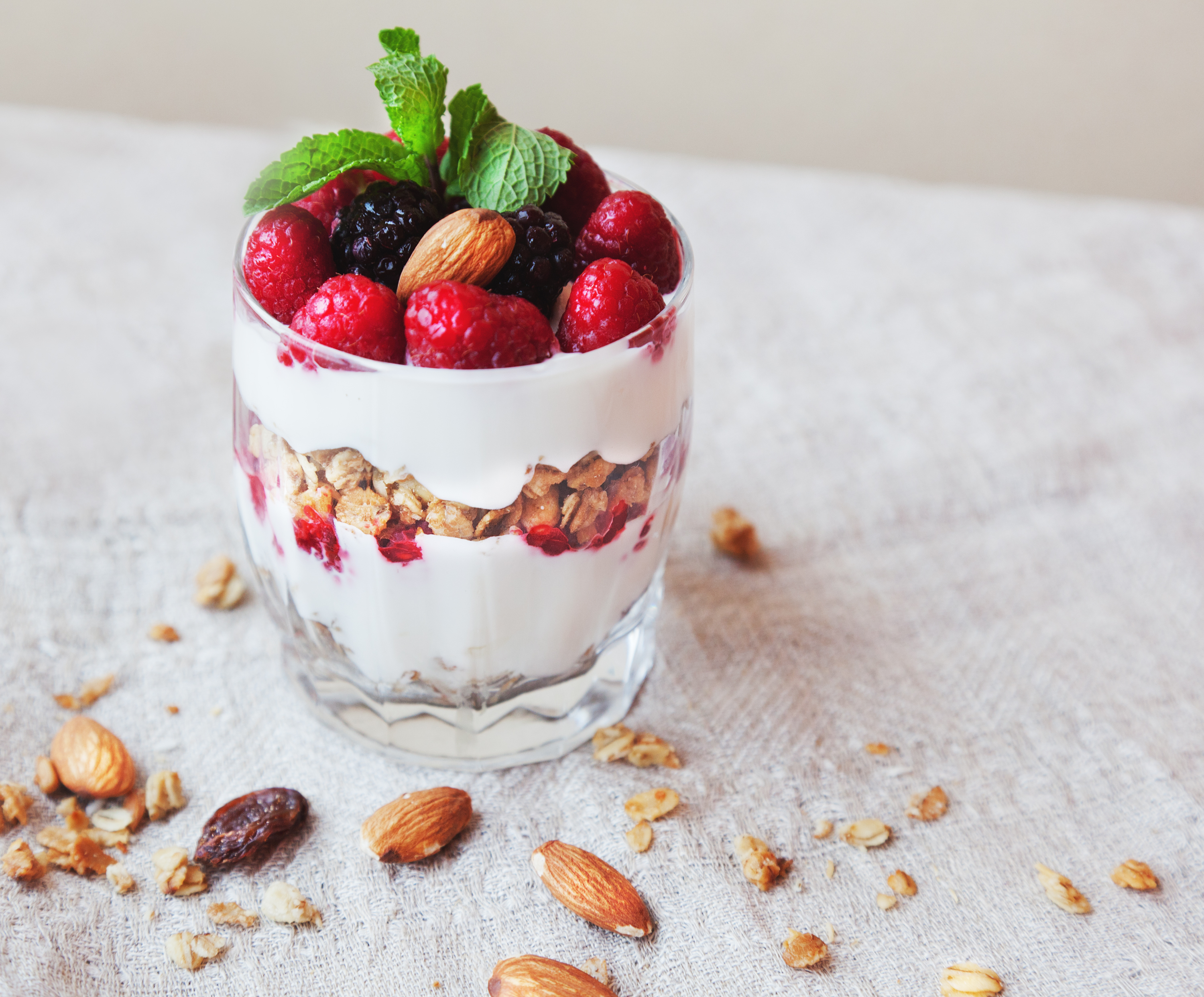 A glass containing yogurt, granola, raspberries, and blueberries.