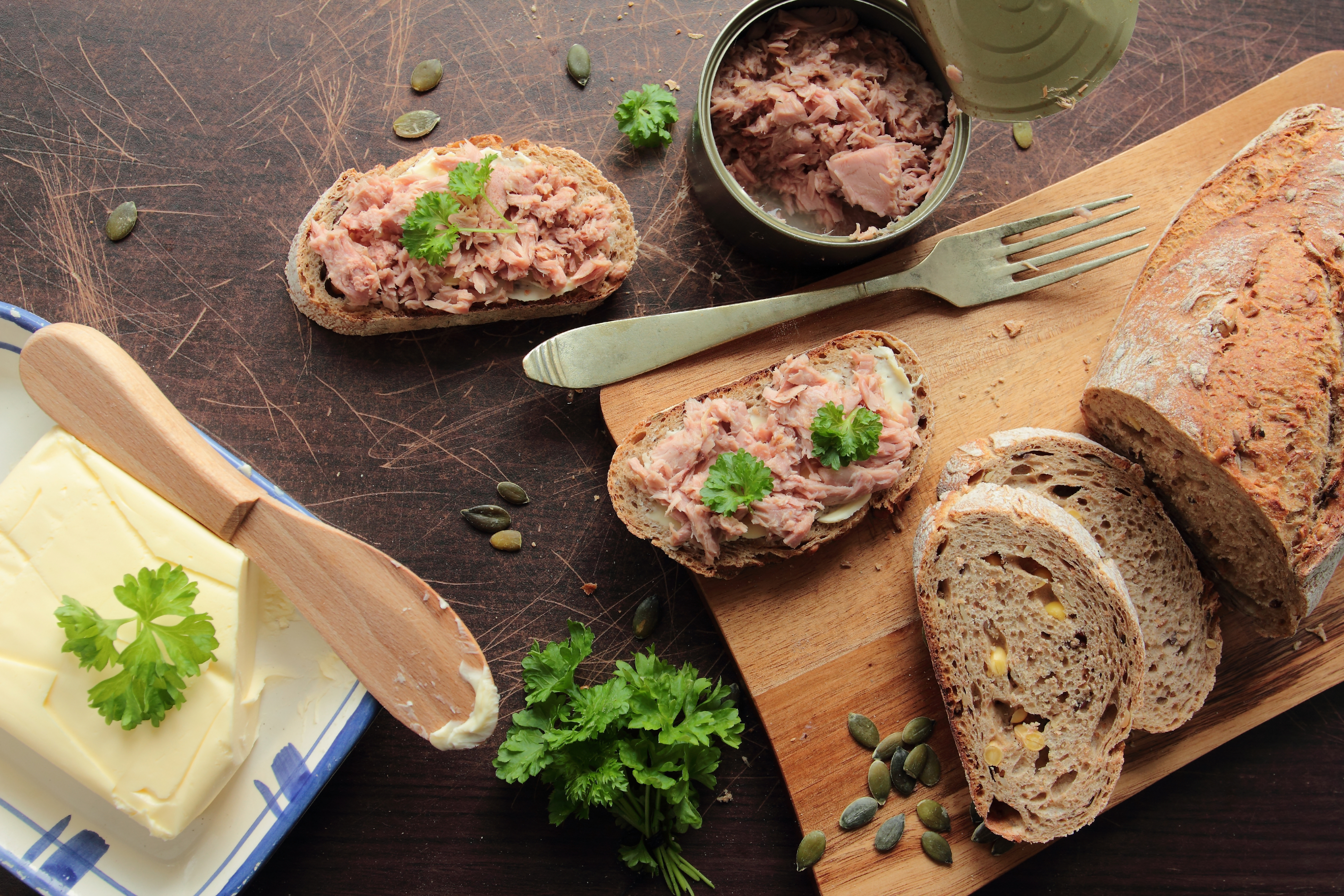 A loaf of bread cut into slices on a cutting board, an opened can of tuna, and two slices of bread topped with the tuna.
