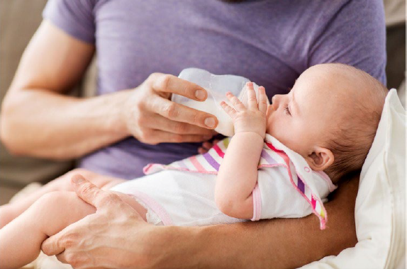 Person feeding an infant from a bottle.