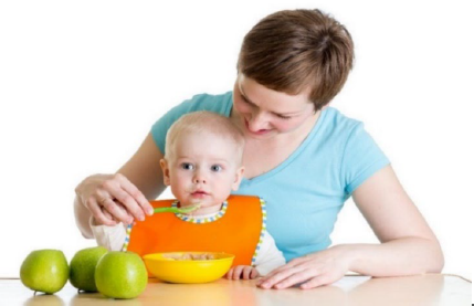 Woman assisting an infant to eat from a spoon.