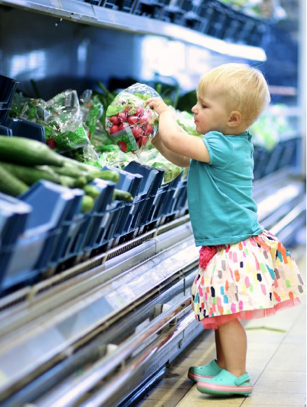 A toddler reaching for produce in a grocery store.