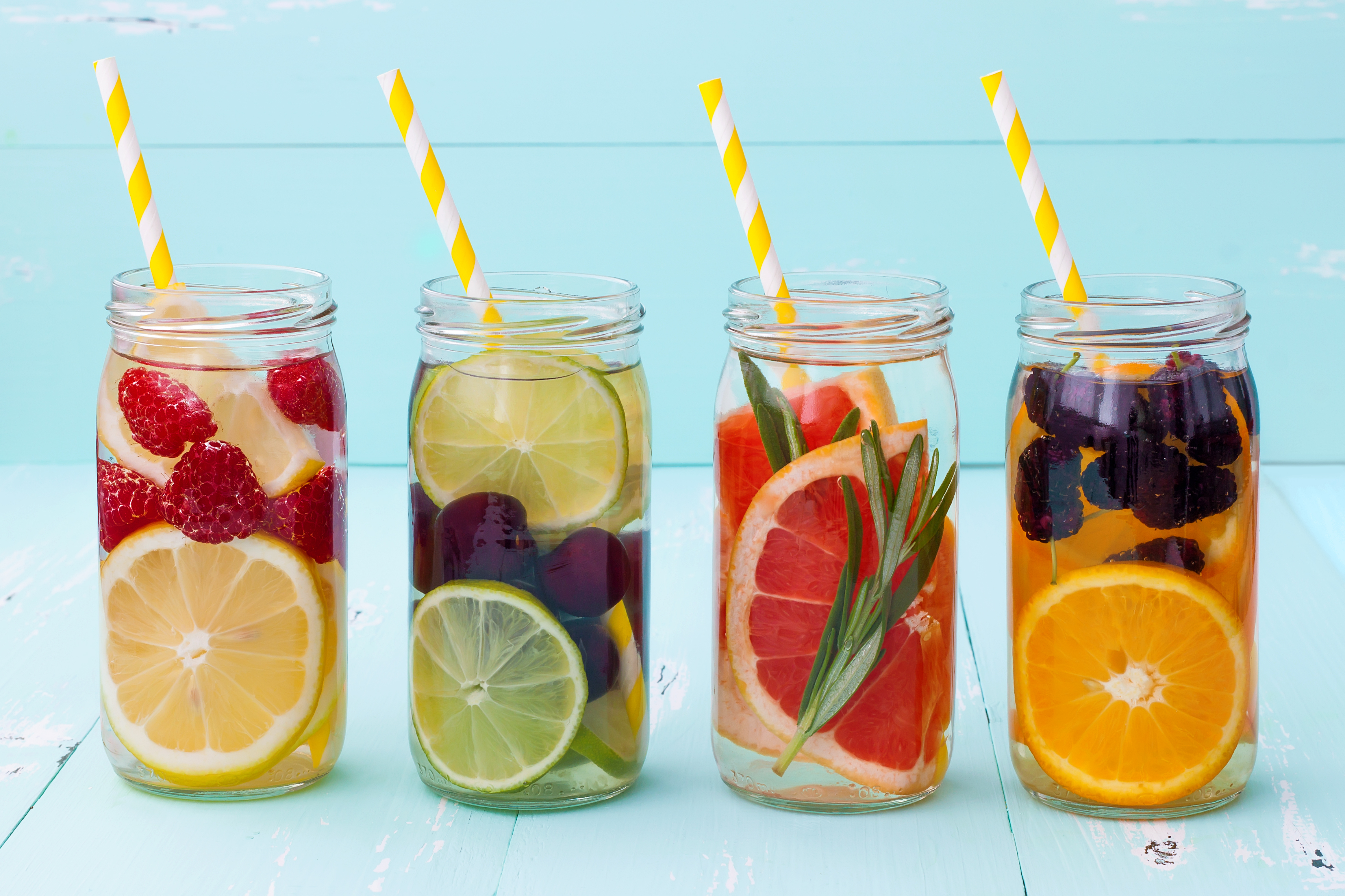Four glass containers filled with various fruits and water and a straw.