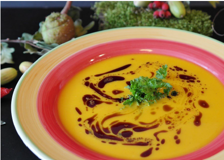 A bowl with orange pumpkin soup with vinegar and herbs on top.