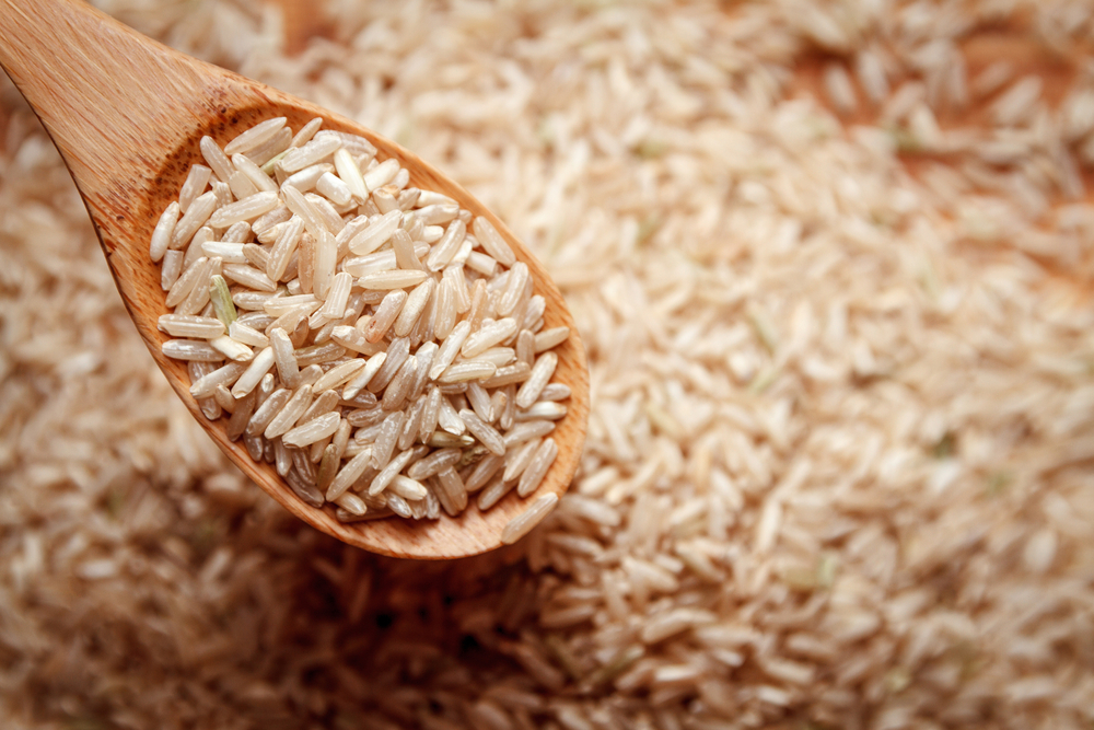 A wooden spoon holding grains of rice above a large pile of rice.