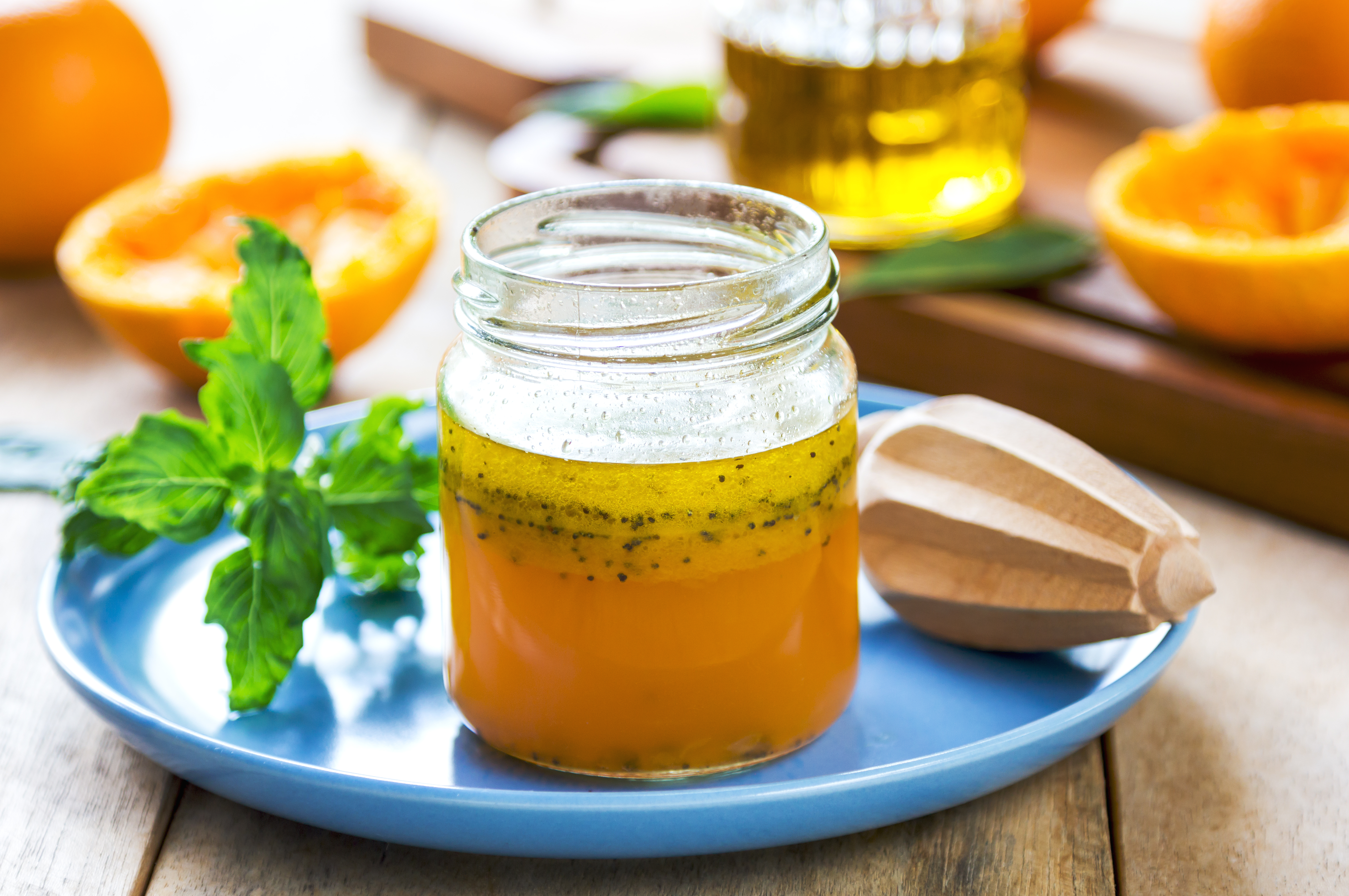 A jar of orange colored salad dressing next to a sprig of a green herb and a wooden orange juicer on top of a blue plate
