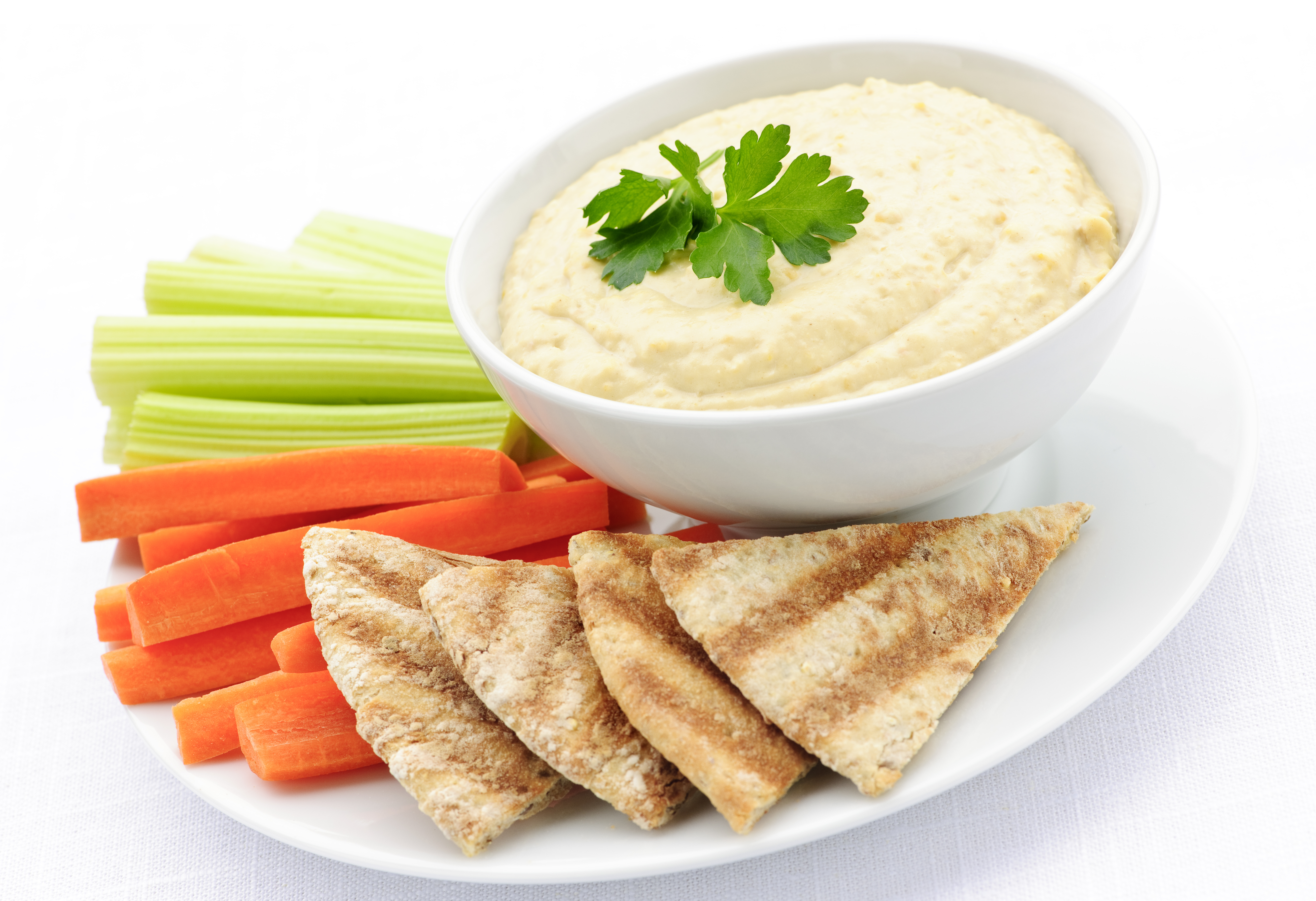 A bowl of hummus with a plate of celery sticks, carrot sticks, and pita bread.
